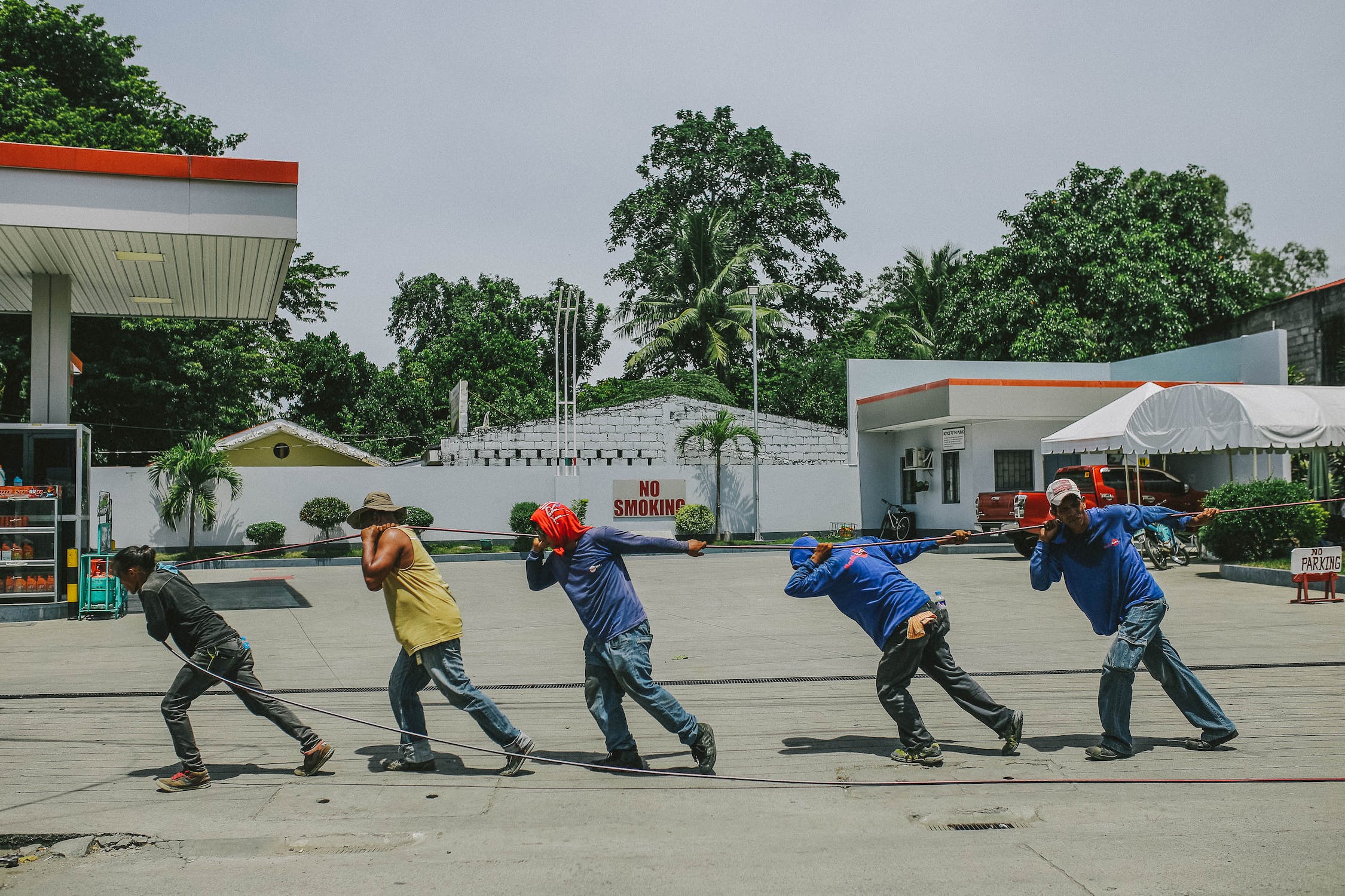 Five men pulling a rope at a gas station